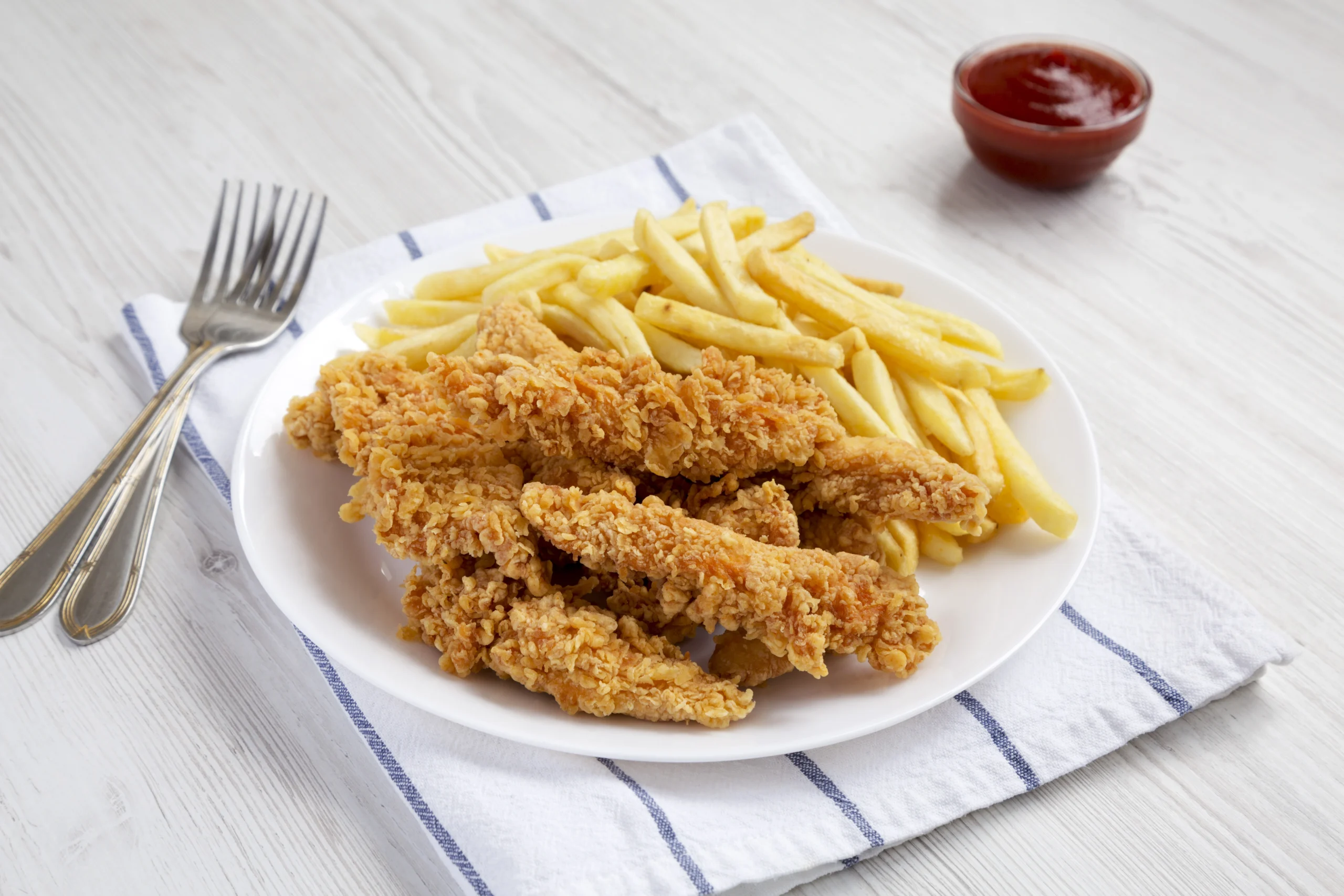 A plate of crispy chicken tenders and golden fries served with dipping sauces, showcasing the ultimate homemade comfort food pairing.